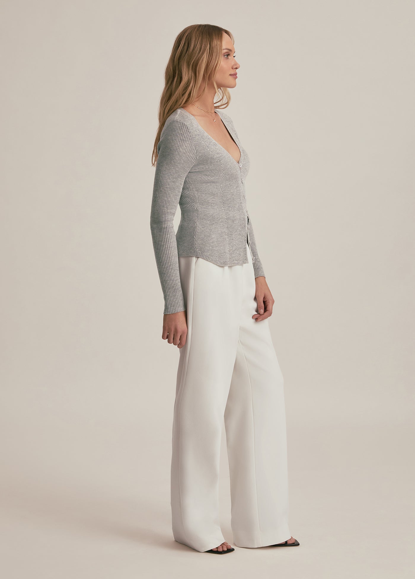 Woman wearing a gray sweater and white pants on a beige background