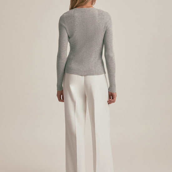 Woman wearing a gray sweater and white pants on a beige background