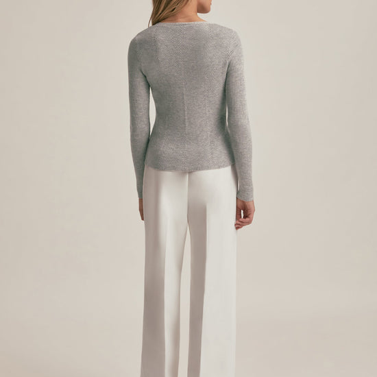 Woman wearing a gray sweater and white pants on a beige background