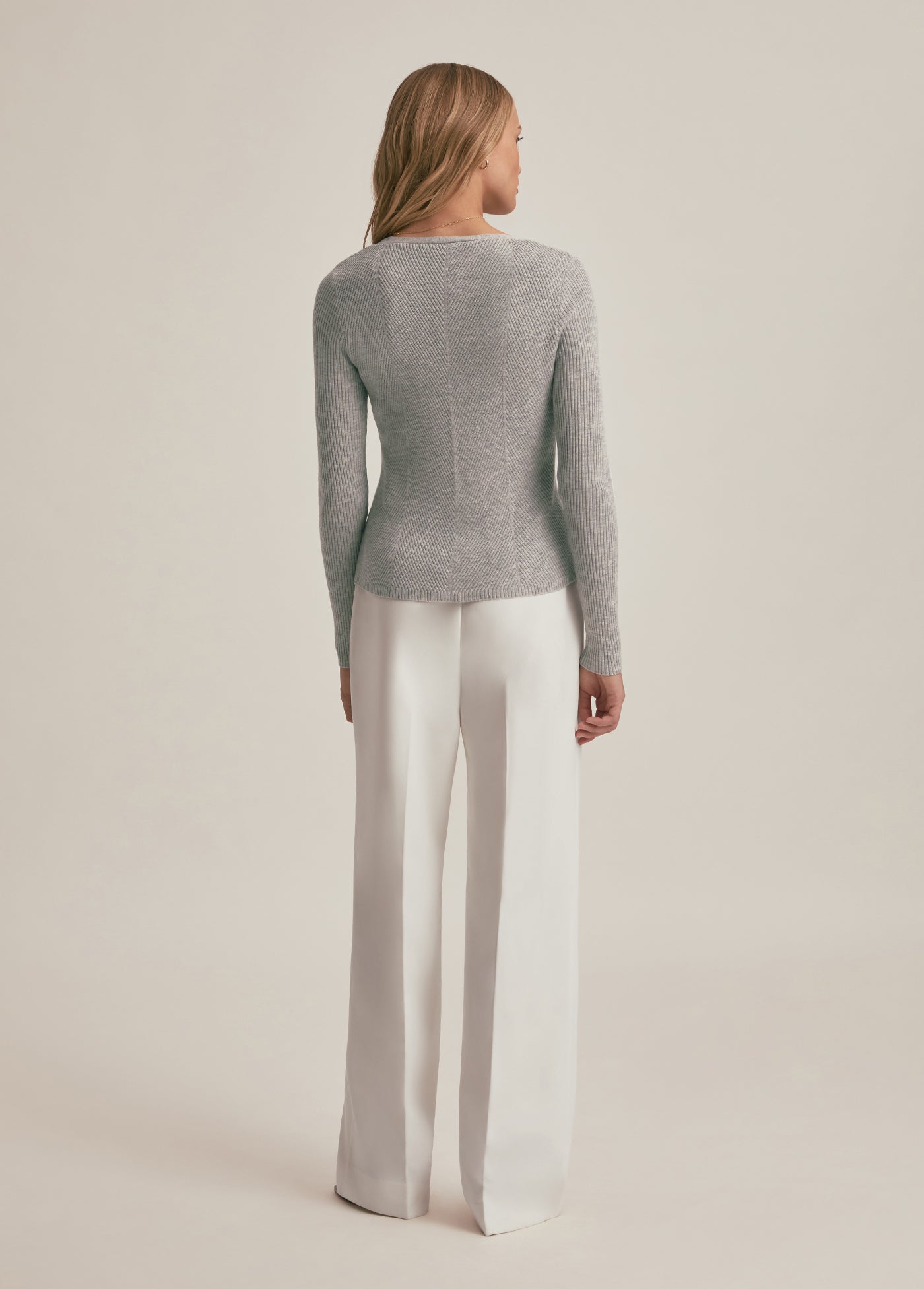 Woman wearing a gray sweater and white pants on a beige background
