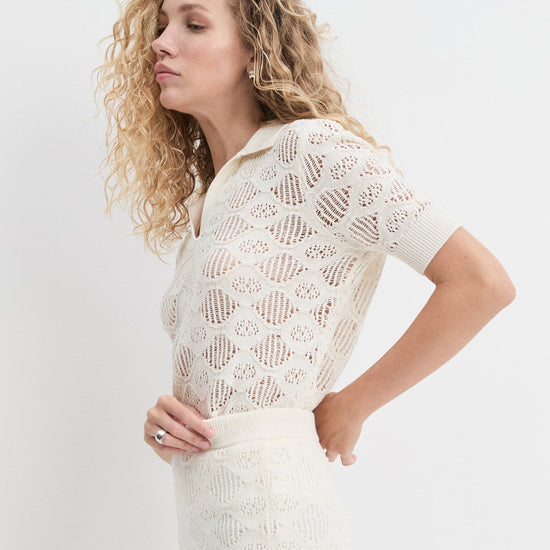 Woman wearing a white lace top and skirt against a plain background