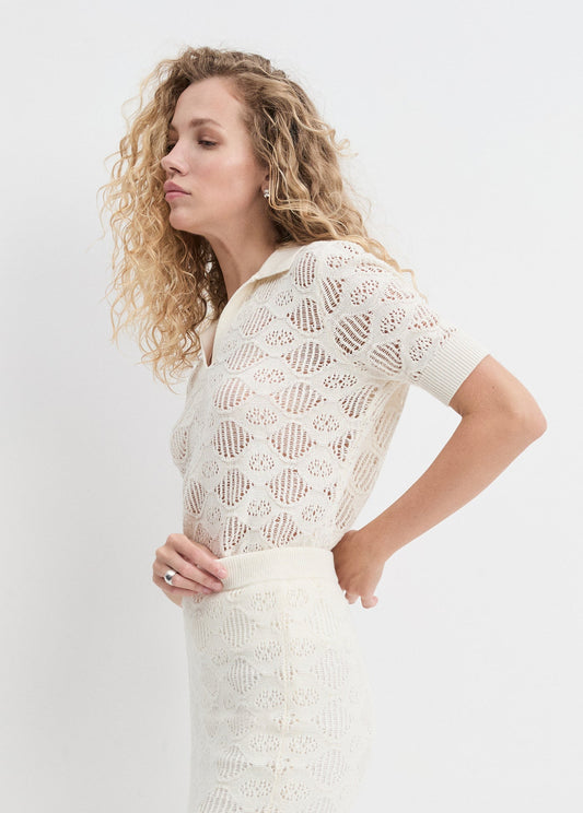 Woman wearing a white lace top and skirt against a plain background