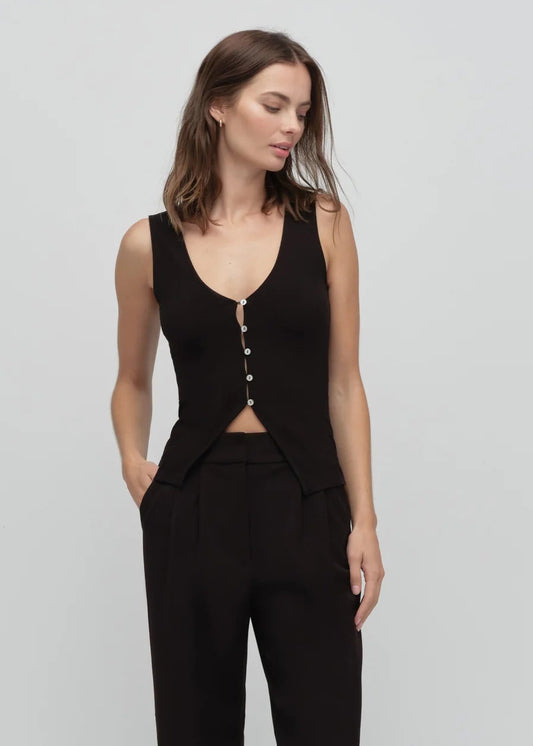 Woman wearing a black sleeveless top with buttons and black pants on a light gray background
