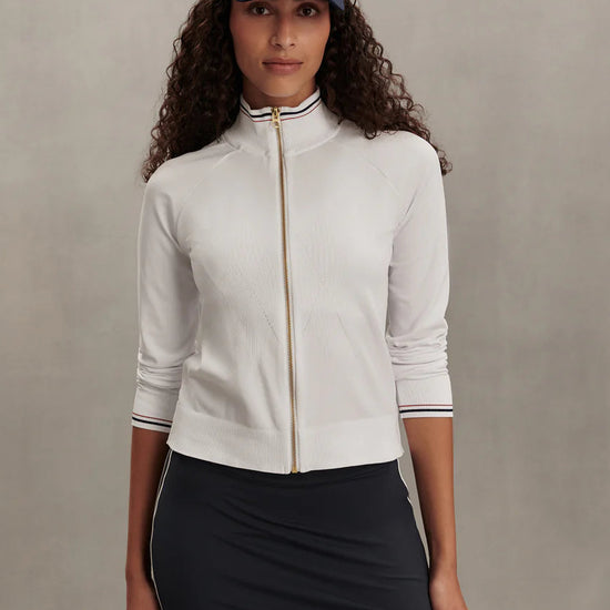 Woman wearing a white long-sleeve top, black skirt, and navy cap with a logo on a beige background