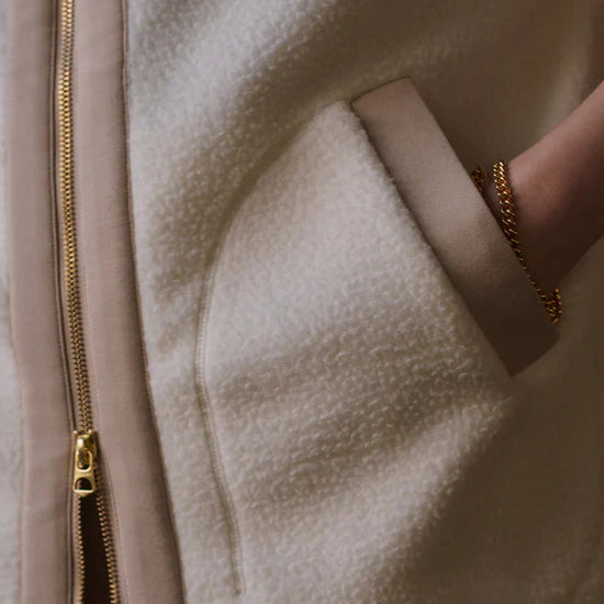 Close-up of a beige fleece jacket with a gold zipper and a hand wearing a gold ring.