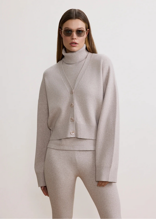 Woman wearing a light gray outfit with a cardigan and pants on a white background